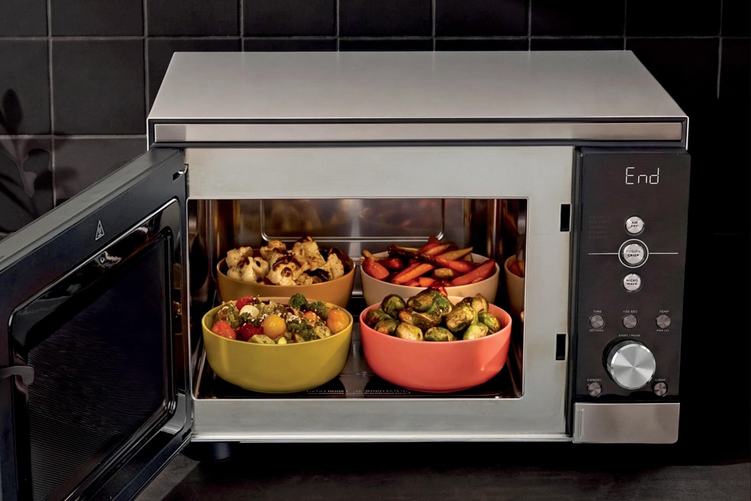 The Ninja Crispi Microwave on a kitchen counter with its door open and four bowls of food inside.