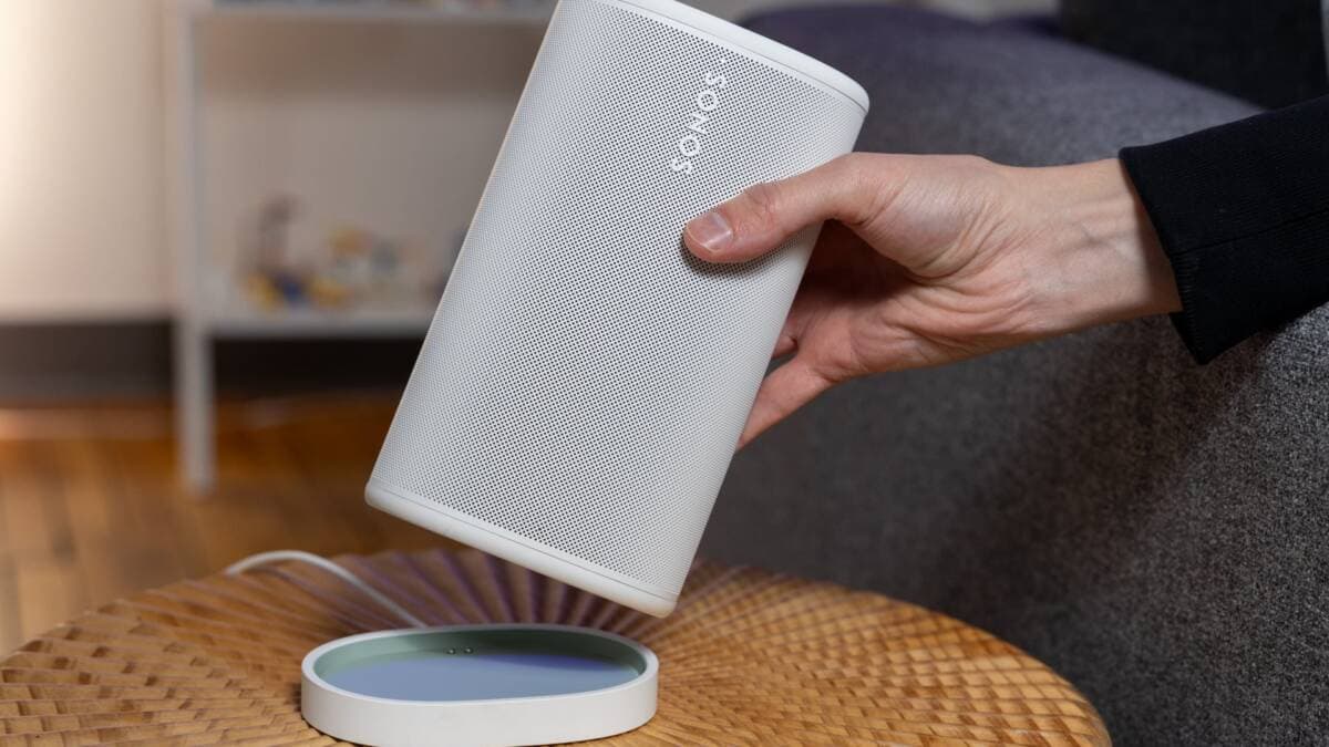 A white Sonos speaker is held in a hand inside a home