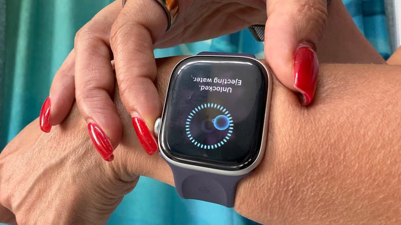 Fingers touching an Apple Watch to eject water.