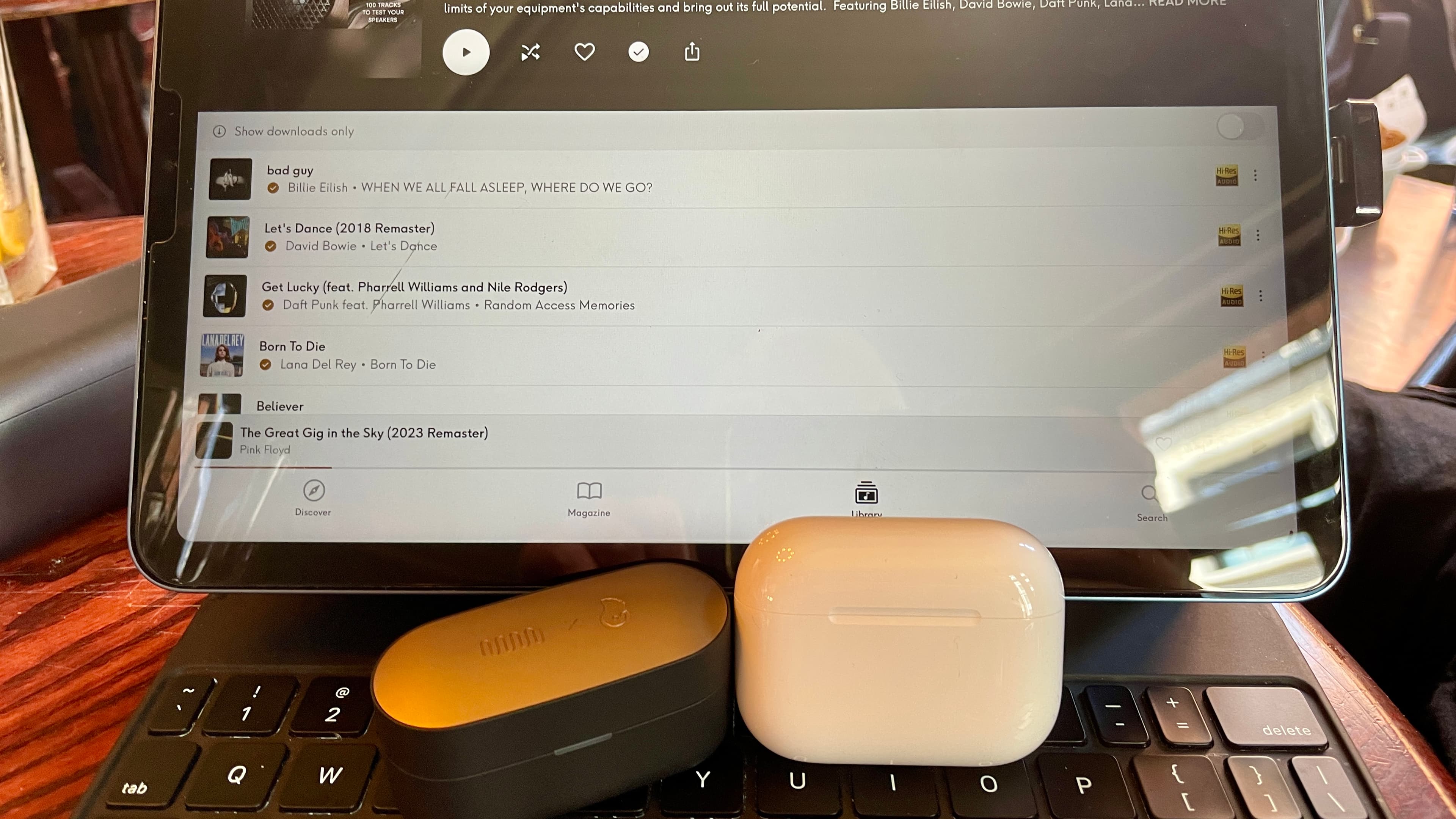 Status Audio Pro X GoldenSound, next to AirPods or held in a hand, with gold accents showing