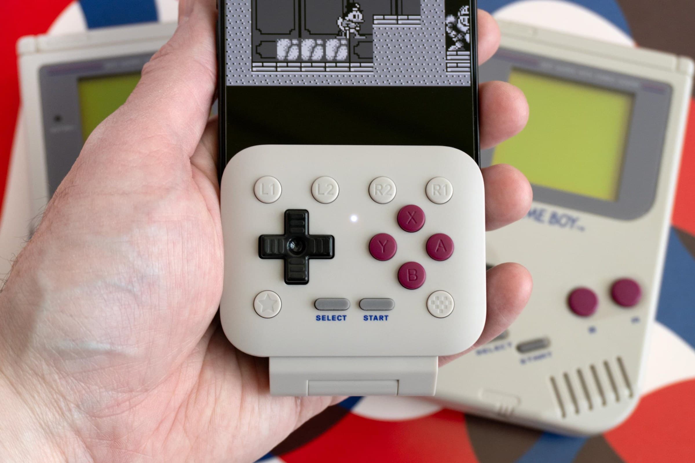 The 8BitDo FlipPad attached to an iPhone held in a person’s hand with a Game Boy game on screen.
