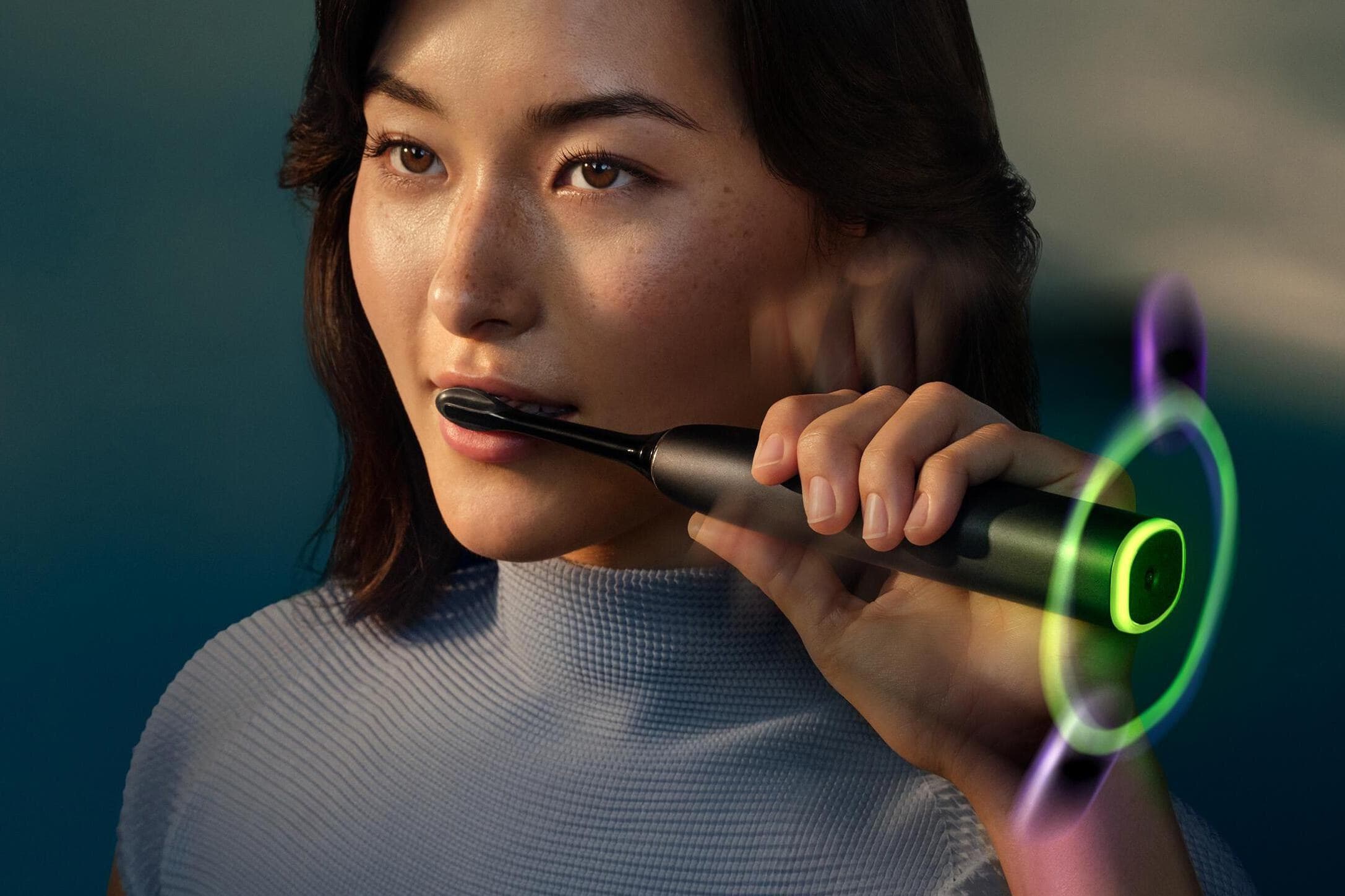 A person brushes with the Philips Sonicare Next-Generation DiamondClean 9900 Prestige smart toothbrush while a glowing ring around its base changes colors.