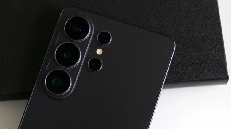 Photo of the camera well of a black Samsung Galaxy S26 Ultra smartphone. The device is placed on a white surface and a black leather mat.