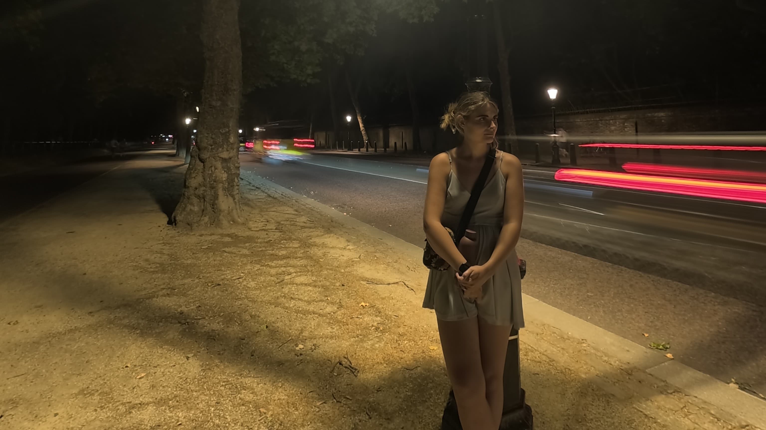 Una mujer junto a una farola por la noche mientras los coches pasan a toda prisa