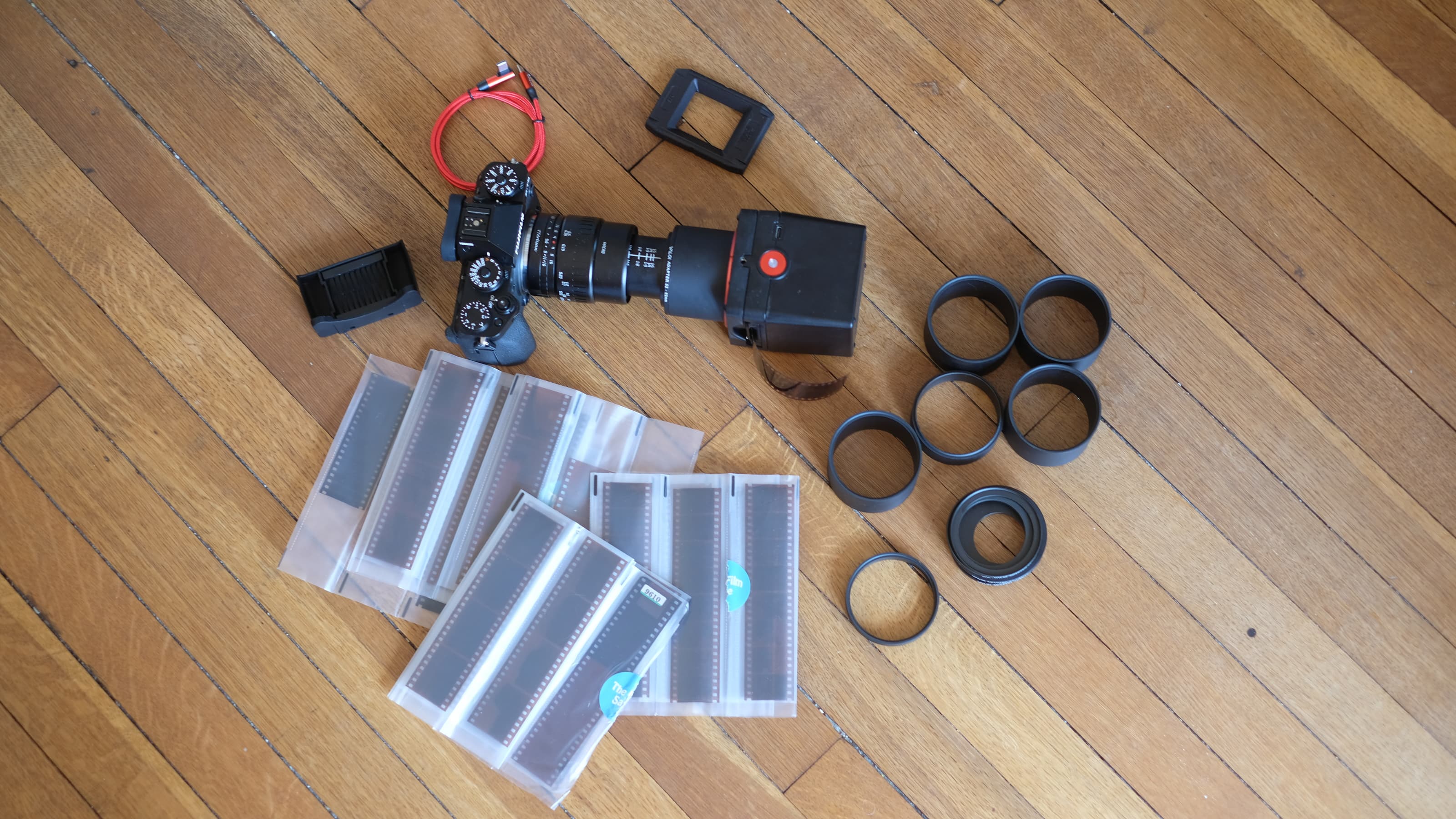 Fotografía del kit Valoi Easy35 V2 dispuesto en el suelo, que incluye cámara, escáner, tubos de extensión, soporte, brocha para el polvo, cable USB y negativos de película