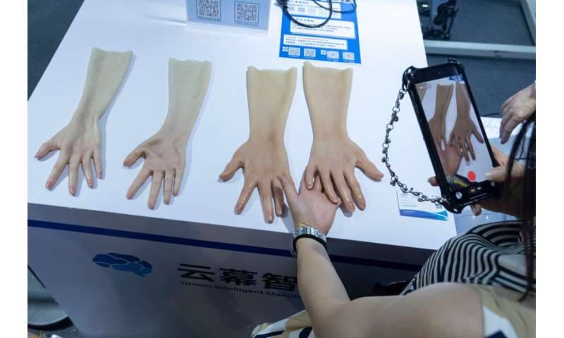 A woman takes photos of realistic skin for robotic hands on display from Yunmu Intelligence Manufacturing during the World AI Conference in Shanghai, Friday, July 17, 2026. Credit: AP Photo/Ng Han Guan