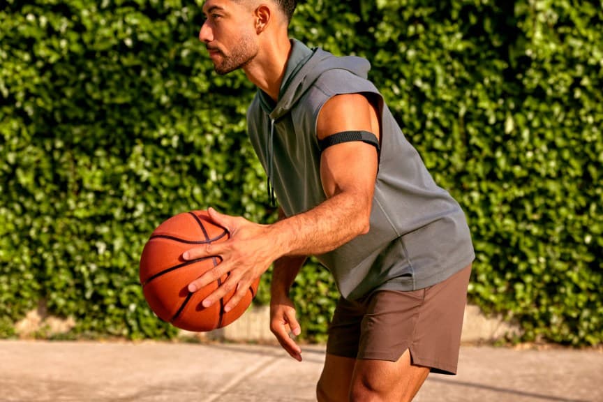 Una persona sosteniendo un balón de baloncesto mientras lleva una banda Cirqa negra en la parte superior del brazo.